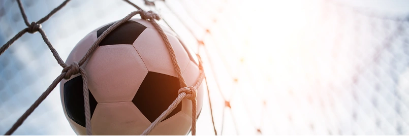Piłka nożna wpadająca do siatki bramki w jasnym świetle stadionowym.